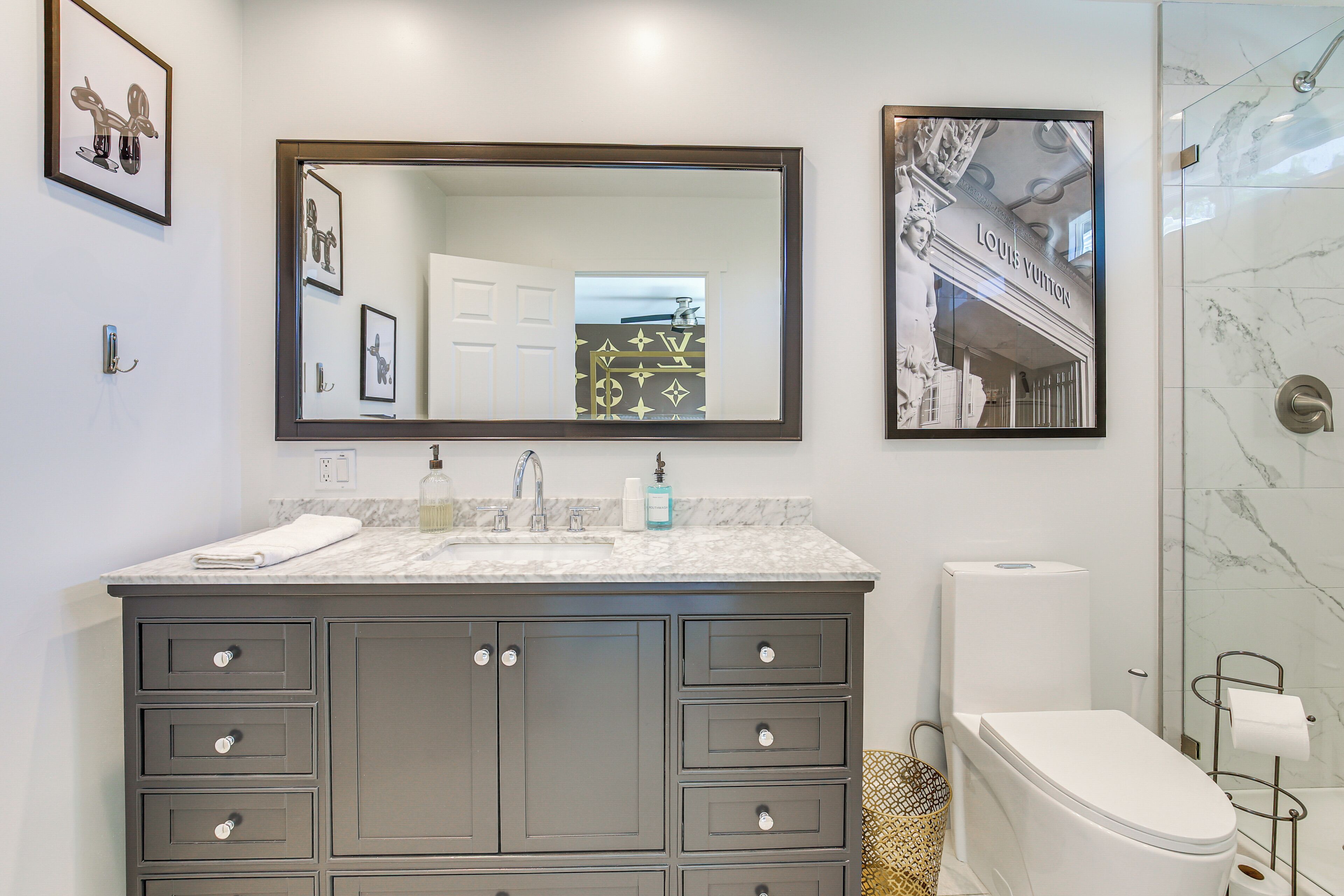 A modern bathroom with a marble countertop, a large mirror, a toilet, and a framed picture of a building.