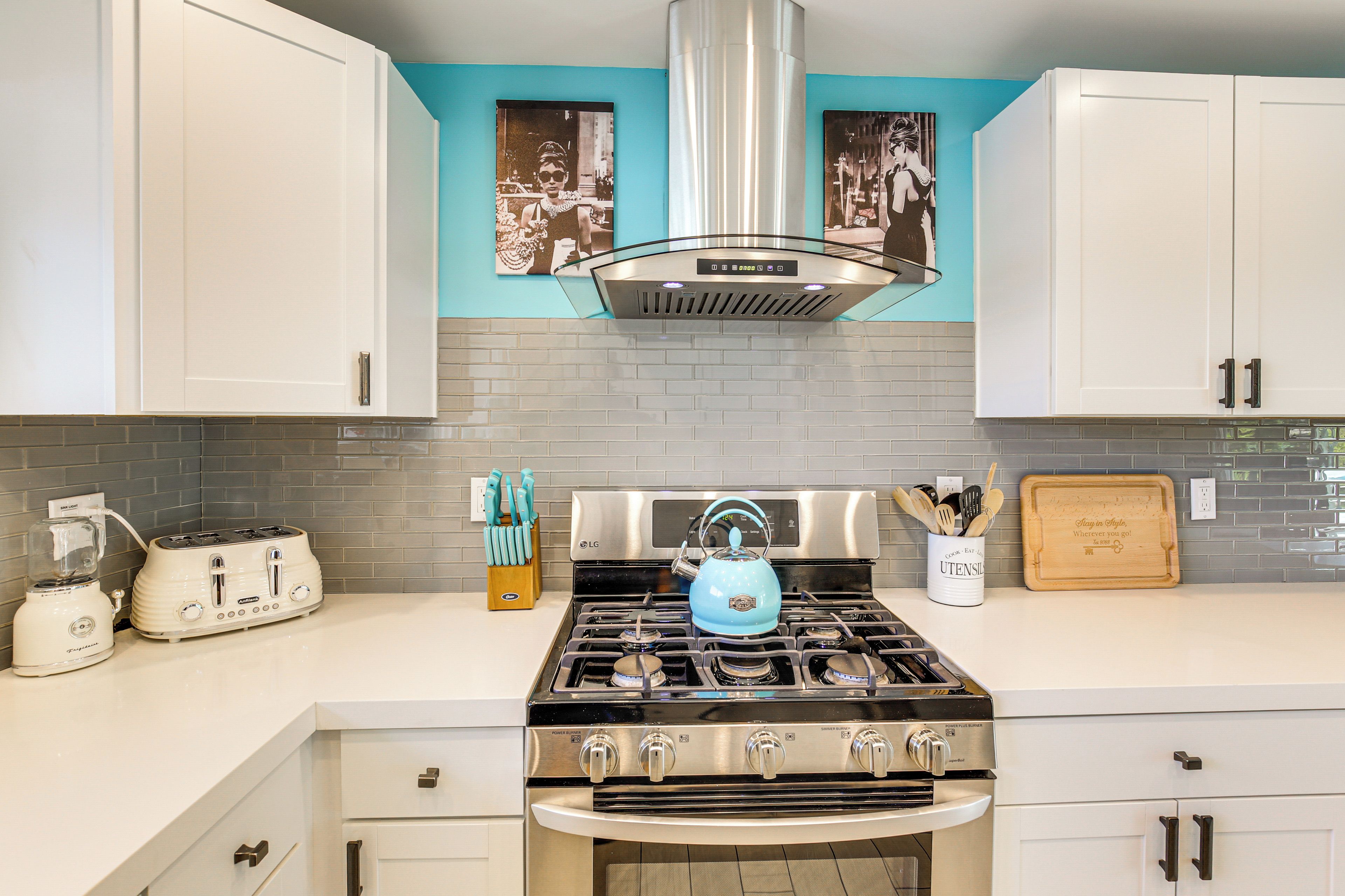 A kitchen with white cabinets, a stainless steel range, a blue kettle, and a toaster.