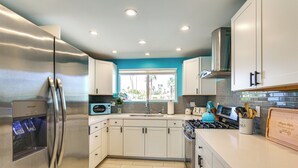 A modern kitchen with stainless steel appliances, white cabinets, and a window with a view of palm trees. - Mtn Views & Outdoor Oasis: Palm Springs Getaway (Palm Springs)