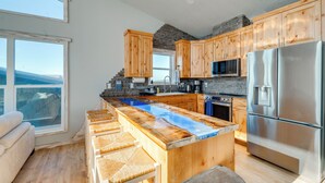 Une cuisine moderne avec des meubles en bois, un grand îlot central, des appareils électroménagers en acier inoxydable et une vue sur les montagnes.