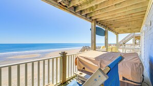 Een houten terras met een bank en een overdekt gedeelte met uitzicht op een strand.