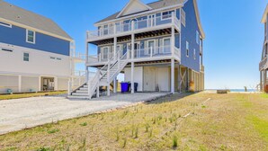 Een tweelaags strandhuis met balkon, trap en zandrijlaan.