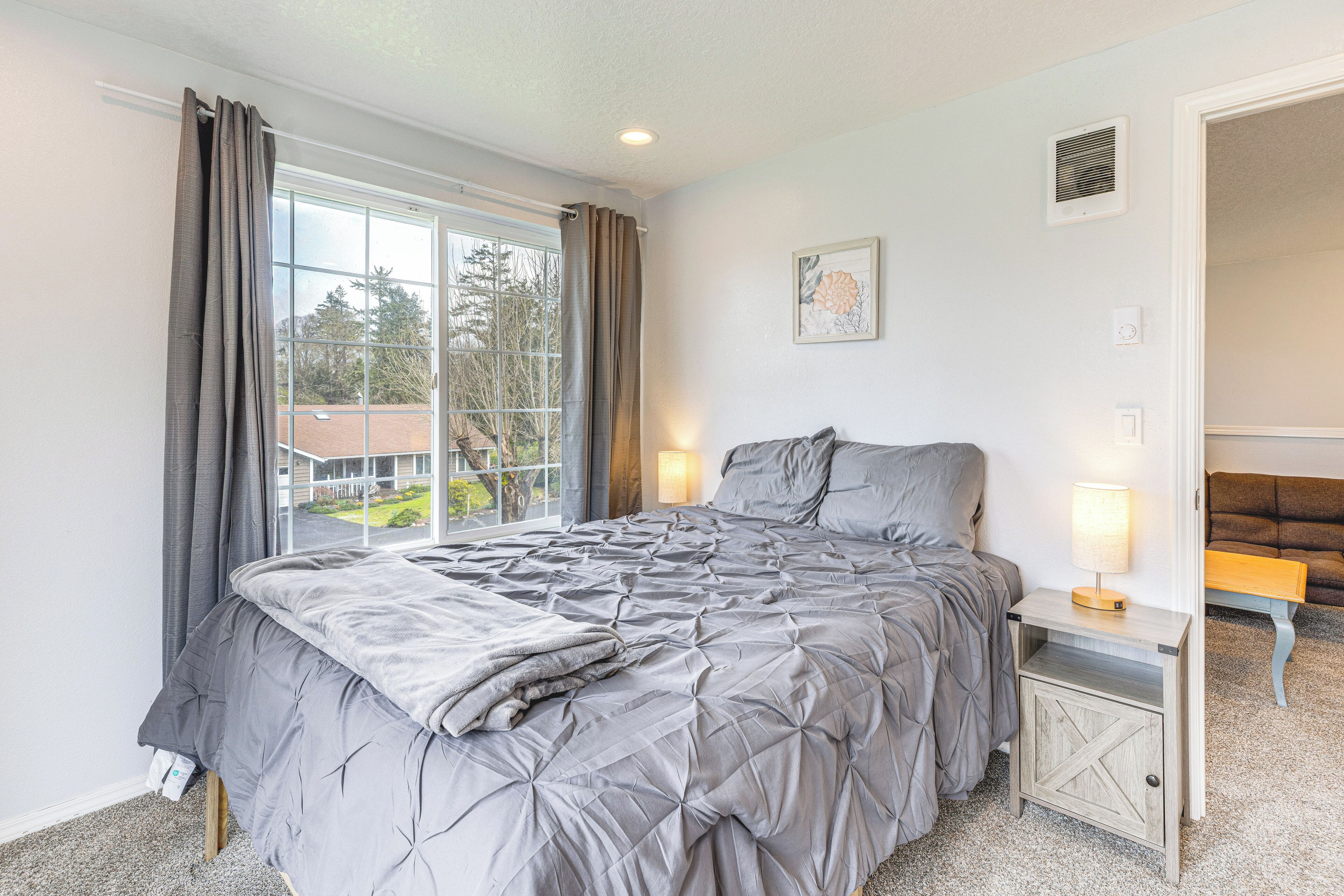 A bedroom with a large bed, a bedside table with a lamp, a window with curtains, and a view of the outside.
