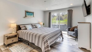 A bedroom with a large bed, a nightstand, a TV, and a view of the outdoors. - 3 Mi to Beach: Oregon North Coast Retreat (Warrenton)