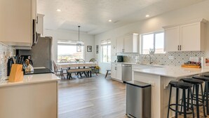 Une cuisine moderne avec des meubles blancs, un grand îlot central doté de tabourets et un coin repas avec une table et des chaises.