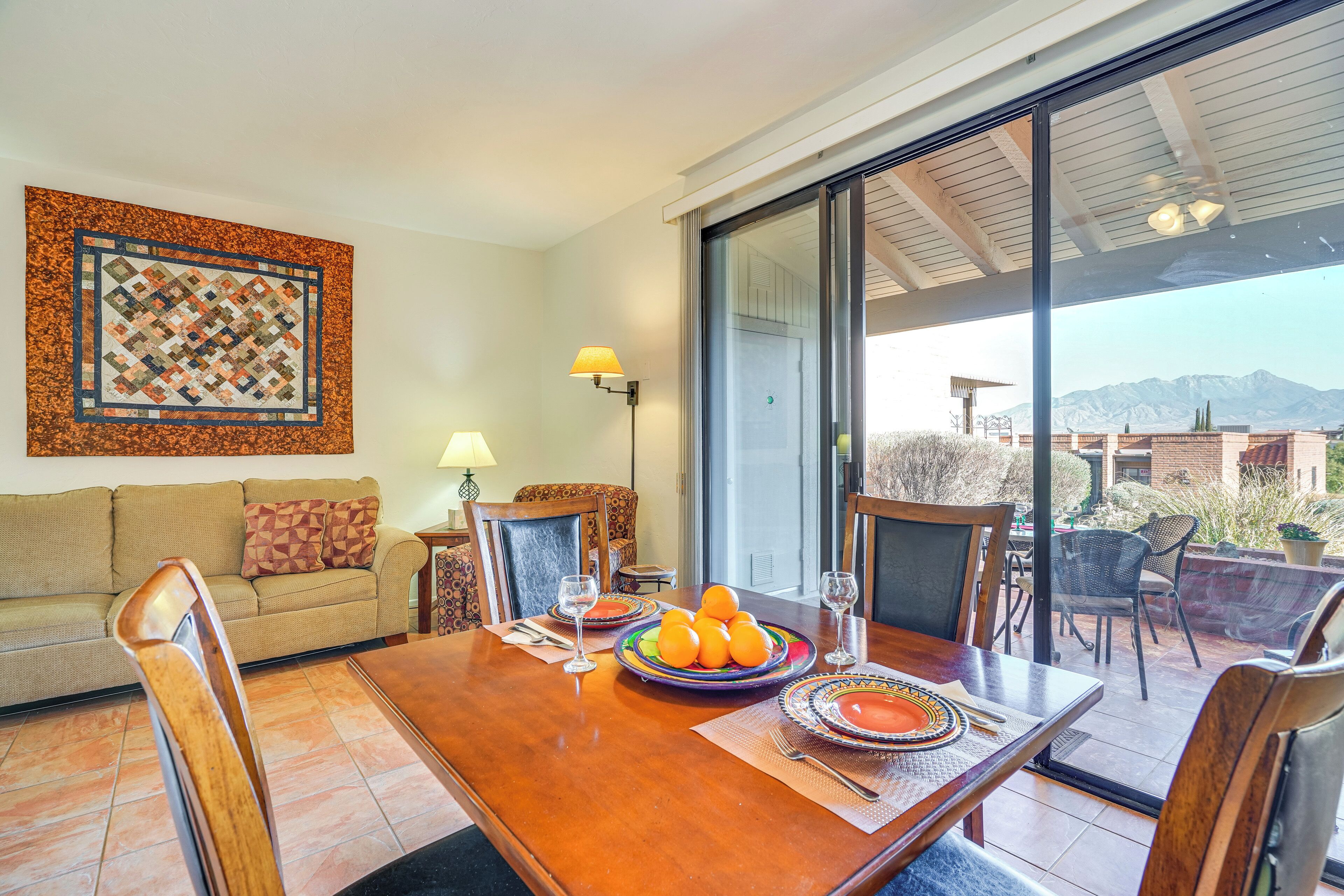 Uma área de refeições com mesa de madeira posta para quatro pessoas, um sofá e uma grande janela com vista para as montanhas.