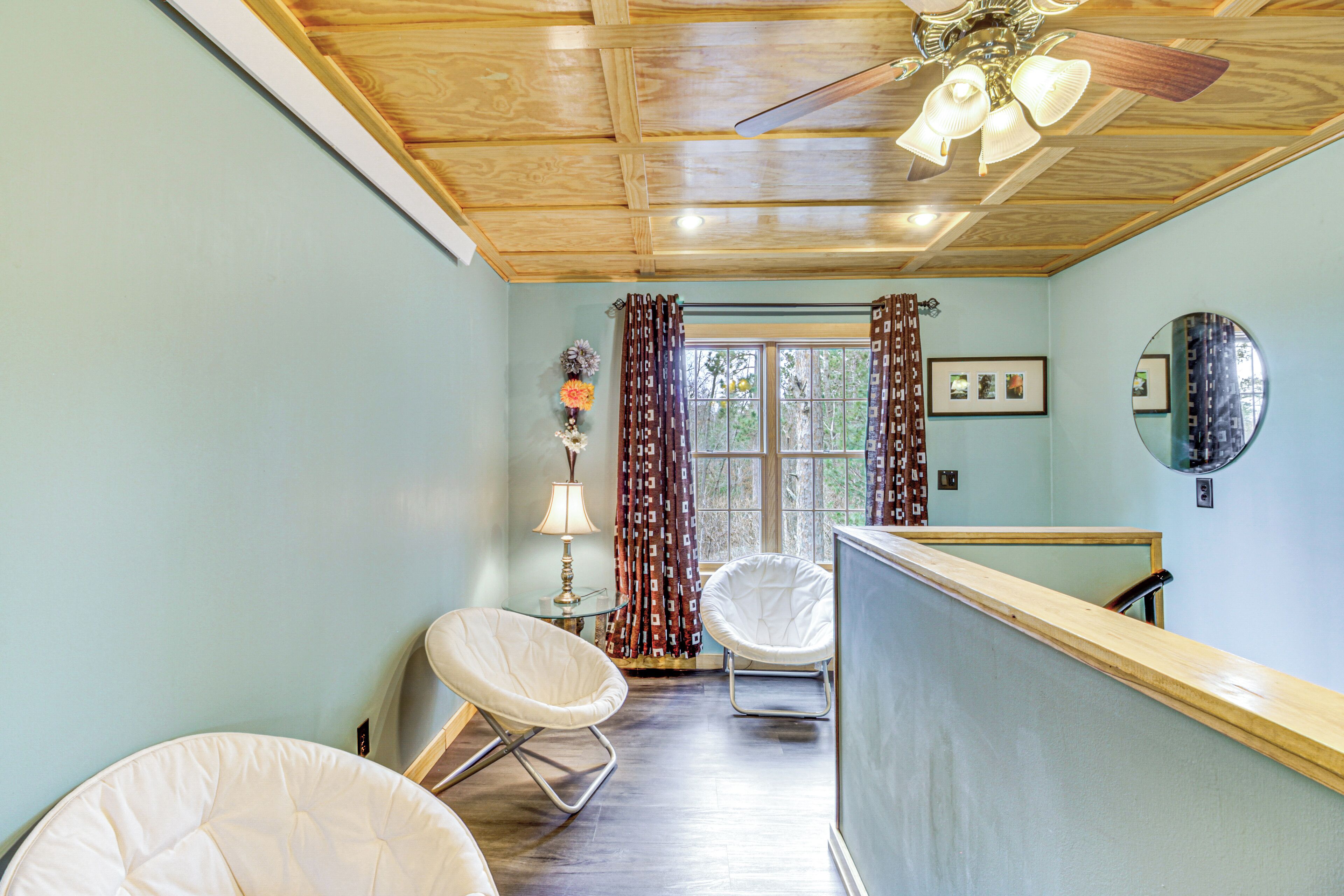 A room with a wooden ceiling, a ceiling fan, a window with curtains, and two white chairs.