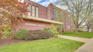 A building named Pershing Heights with a brick facade, a covered walkway, and a well-maintained lawn.