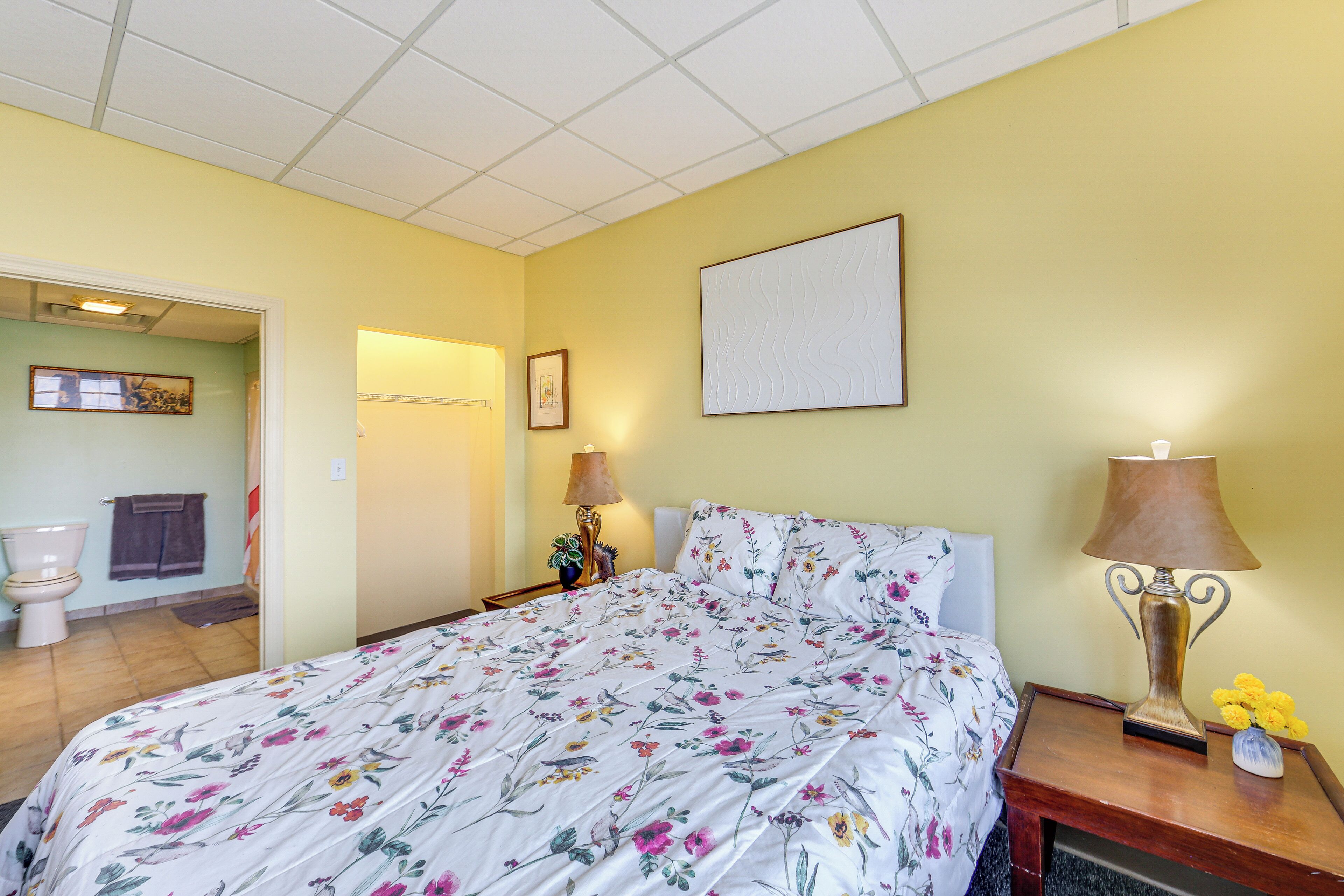 Une chambre à coucher avec une couvre-lit à motifs floraux, une lampe de chevet et une table de nuit ornée d’un vase de fleurs.
