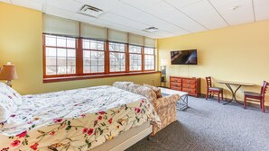 A hotel room with a bed, a desk, a chair, a television, and a window with blinds.