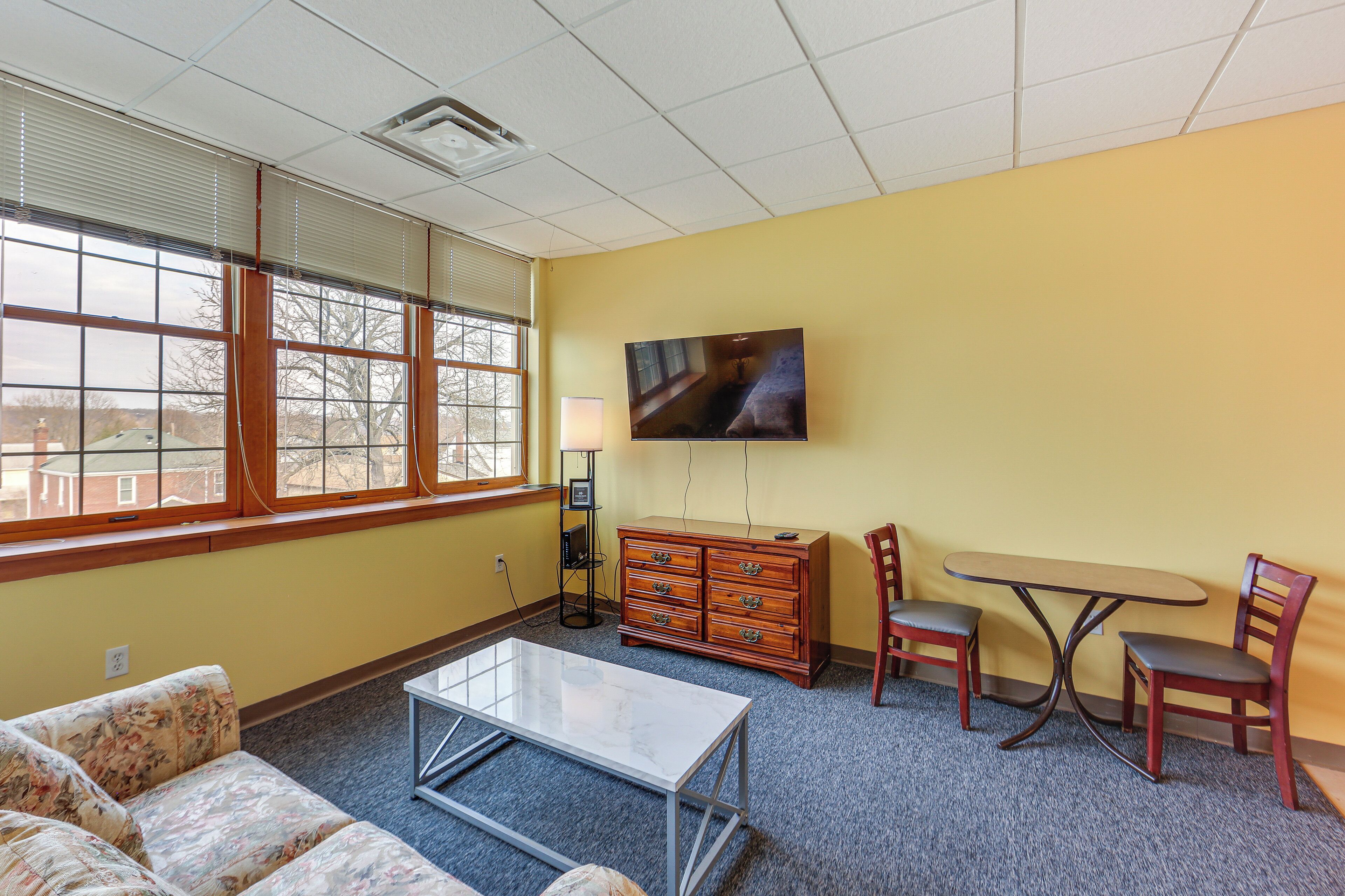 A room with a sofa, a coffee table, a TV, a dresser, and a small table with chairs.