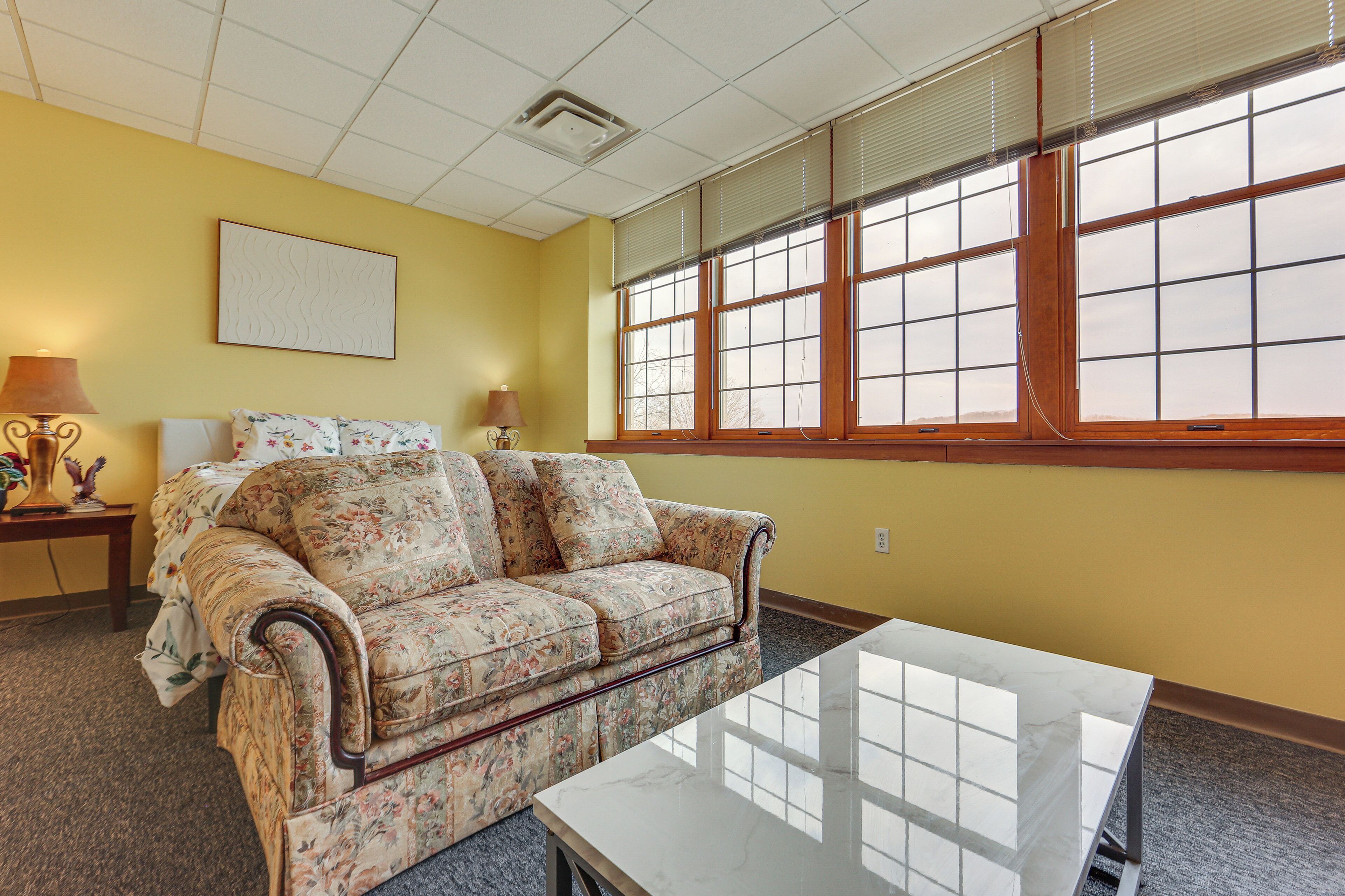 A room with a floral sofa, a white table, and a large window with blinds.