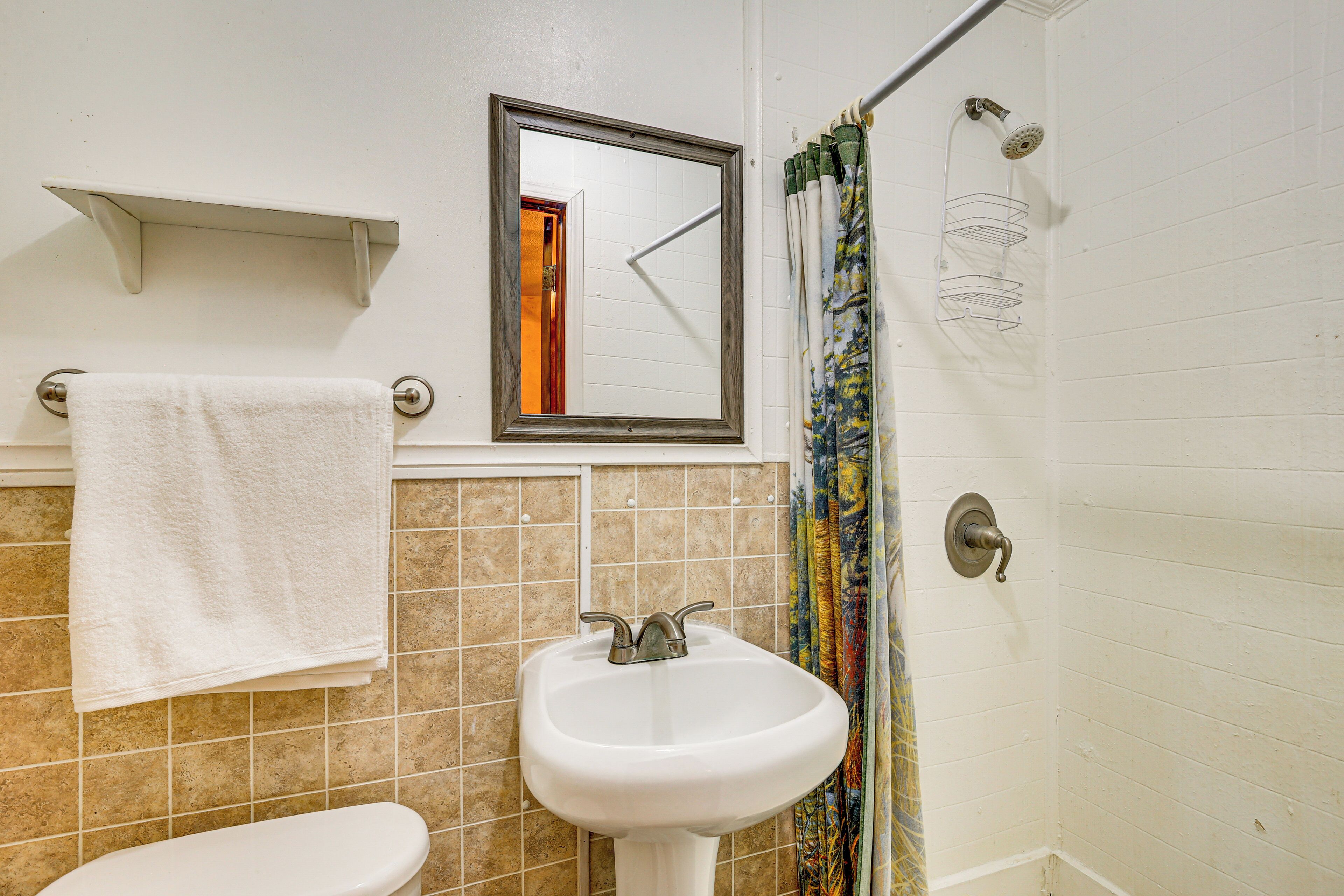 Een badkamer met een witte wastafel, toilet, spiegel en douchegordijn.