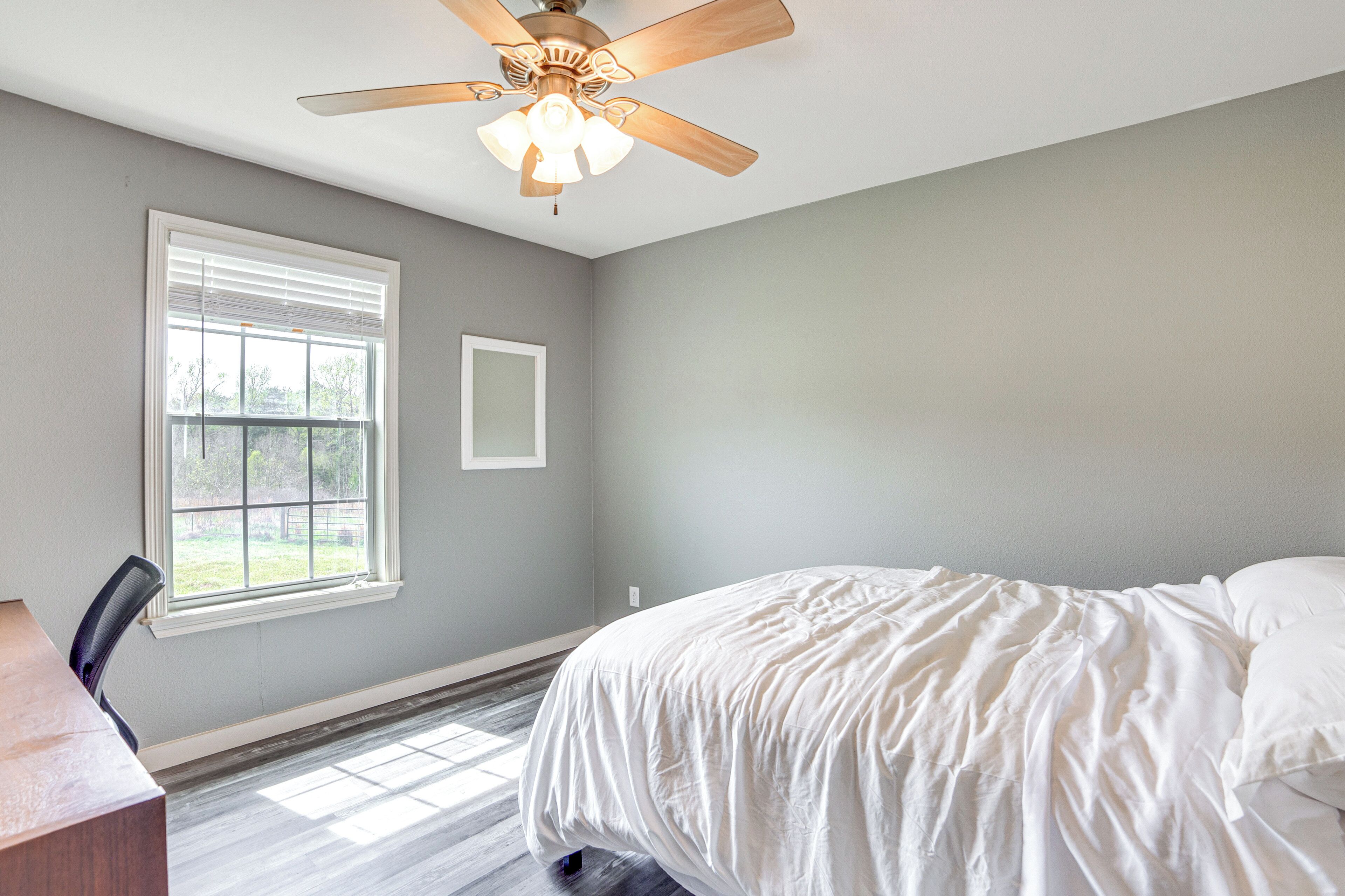 A bedroom with a bed, a ceiling fan, a window, and a desk.
