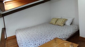 Ein kleines Zimmer mit einem Einzelbett, geneigter Decke und Holzbalken.
