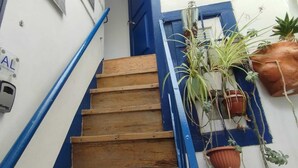 Eine Holztreppe mit blauen Geländern, begrenzt von weißen Wänden mit einigen gerahmten Bildern und einem Schild.