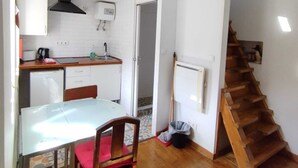 Eine kleine Küche mit weißen Schränken, einem Holztisch und einer Treppe, die in ein Obergeschoss führt.