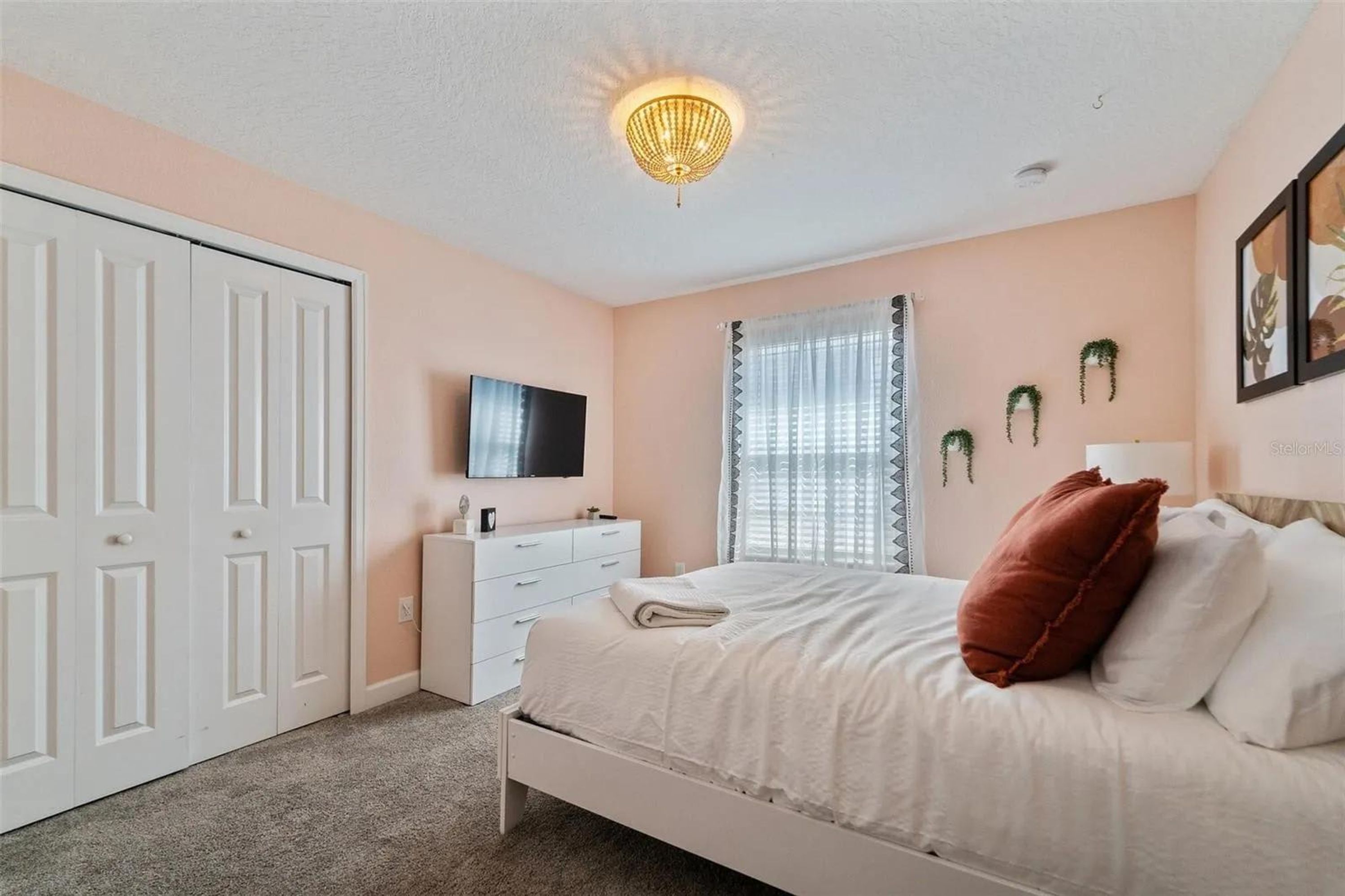 A bedroom with a bed, a dresser, a TV, a window with curtains, and a door.