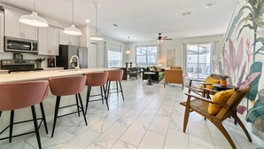 A modern kitchen with white cabinets, a central island with bar stools, and a dining area with a sofa and chairs.