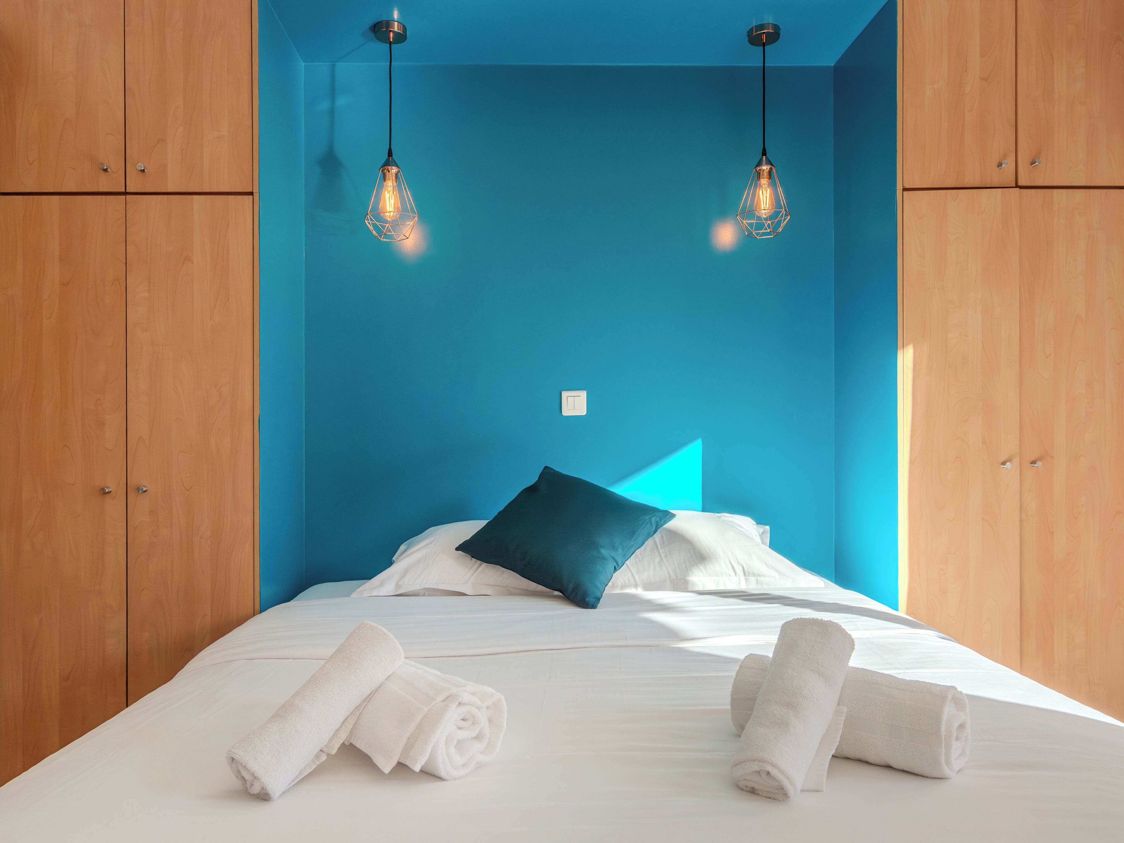 Une chambre d’hôtel avec un lit, deux lampes, un mur bleu et des armoires en bois.