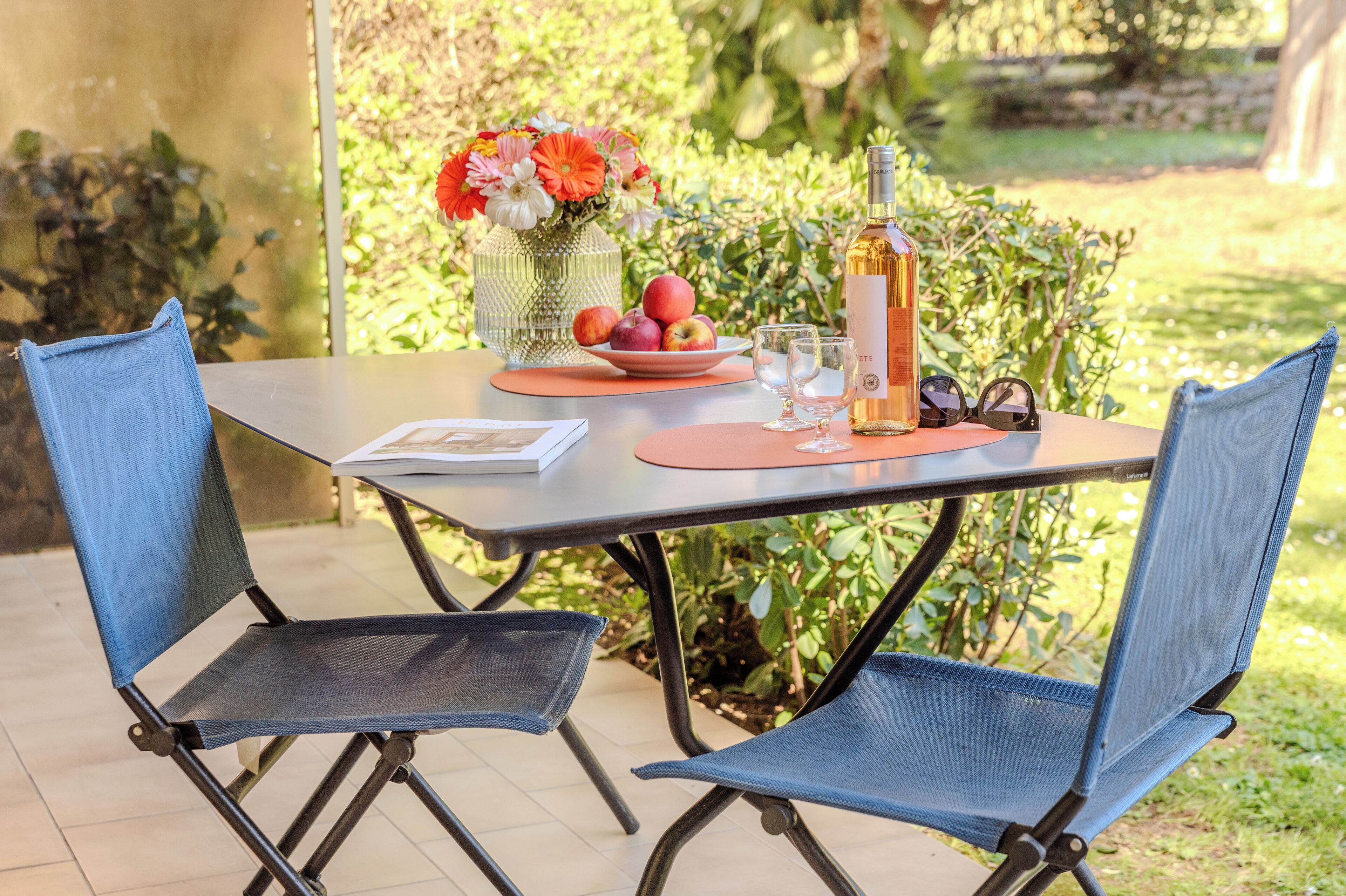 Une table avec un livre, une bouteille, des verres et une assiette de fruits.