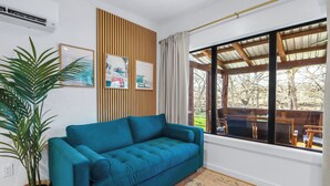 Un sofá turquesa en una habitación con un ventanal grande, una planta en maceta y dos cuadros en la pared.