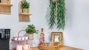 Una encimera de cocina con una cafetera Keurig, un reposa vasos rosa, una botella de vino y una bandeja de mimbre con vasos.