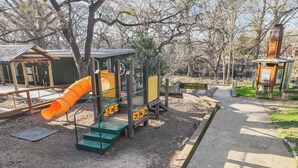 Un terrain de jeux équipé d’un toboggan et de structures d’escalade, entouré d’arbres et bordé d’un sentier de découverte de la nature.