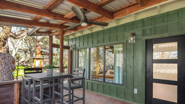 Une terrasse couverte avec une table et des chaises, un ventilateur de plafond et une vue sur l’extérieur.