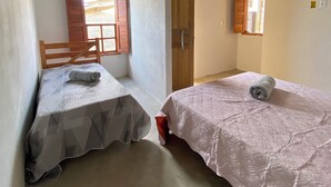 Una habitación pequeña y acogedora con dos camas, techo de madera y una ventana con contraventanas.