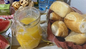 Een tafel met een glazen karaf sinaasappelsap, een broodmand en diverse etenswaren, waaronder een pak koekjes en een melkverpakking.