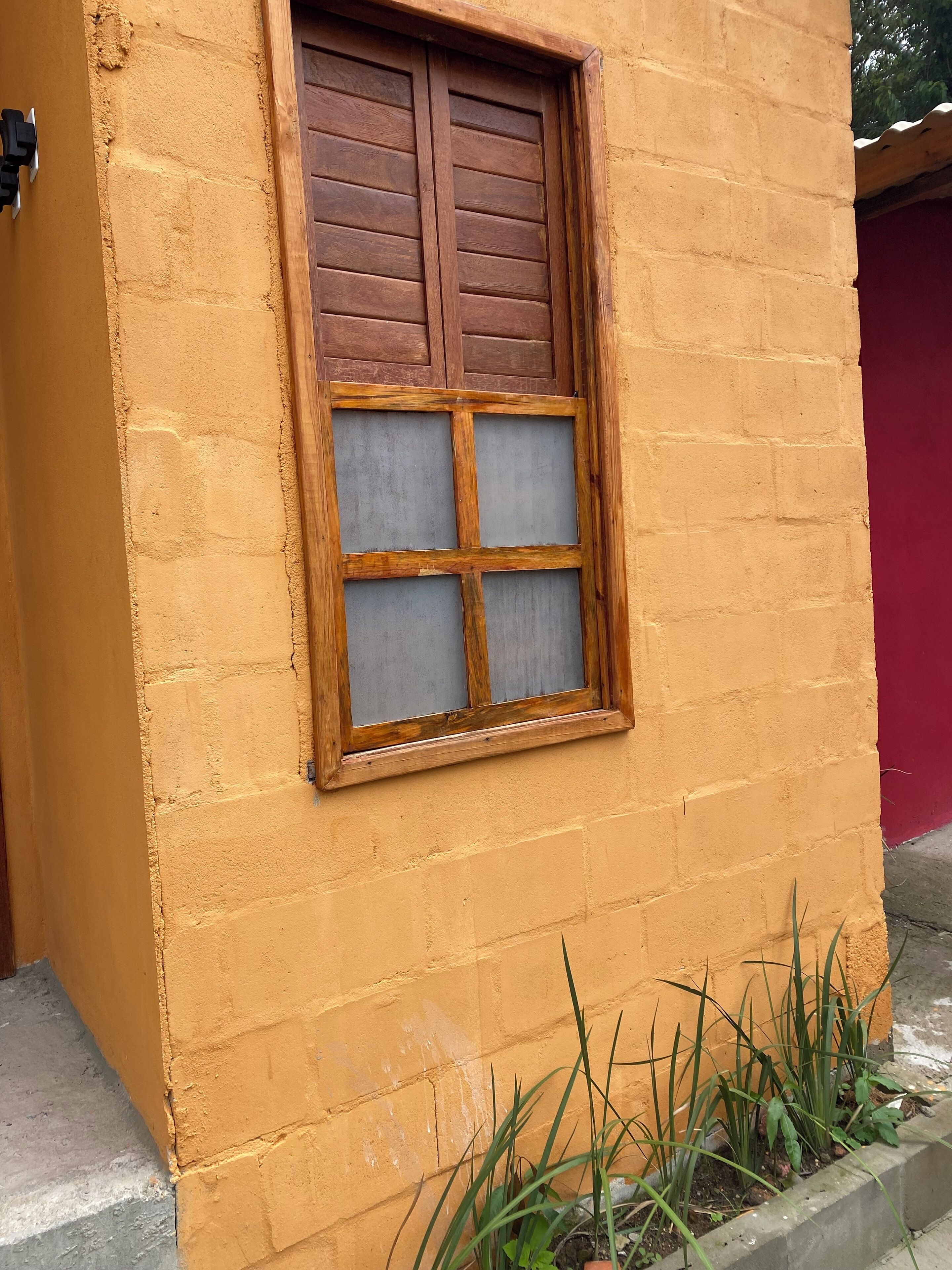 A window with wooden shutters and a grid pattern, set in a yellow brick wall.