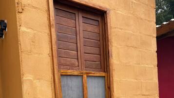A window with wooden shutters and a grid pattern, set in a yellow brick wall.
