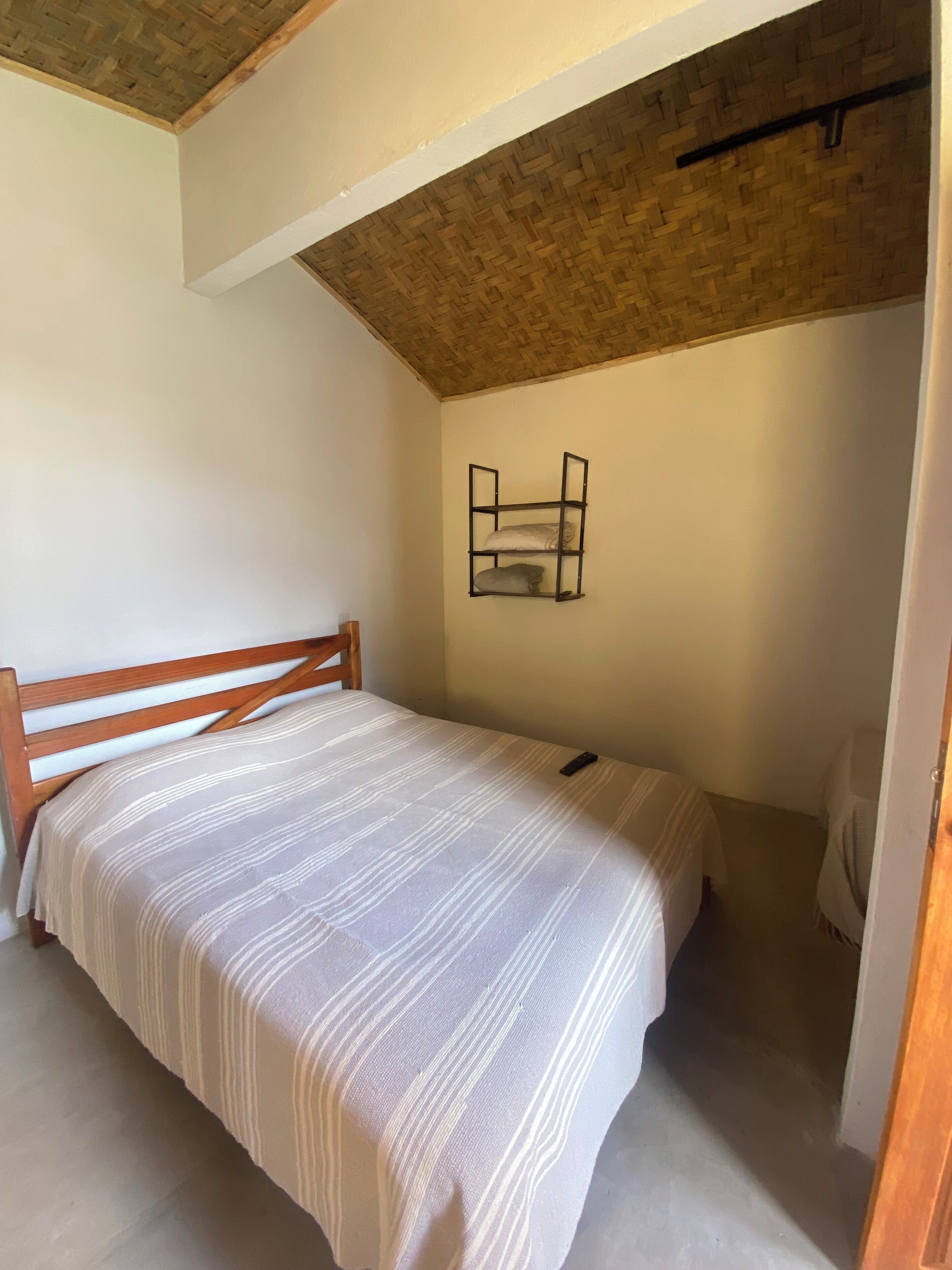 Une chambre à coucher avec un cadre de lit en bois, une couvre-lit à rayures et une étagère avec des coussins.