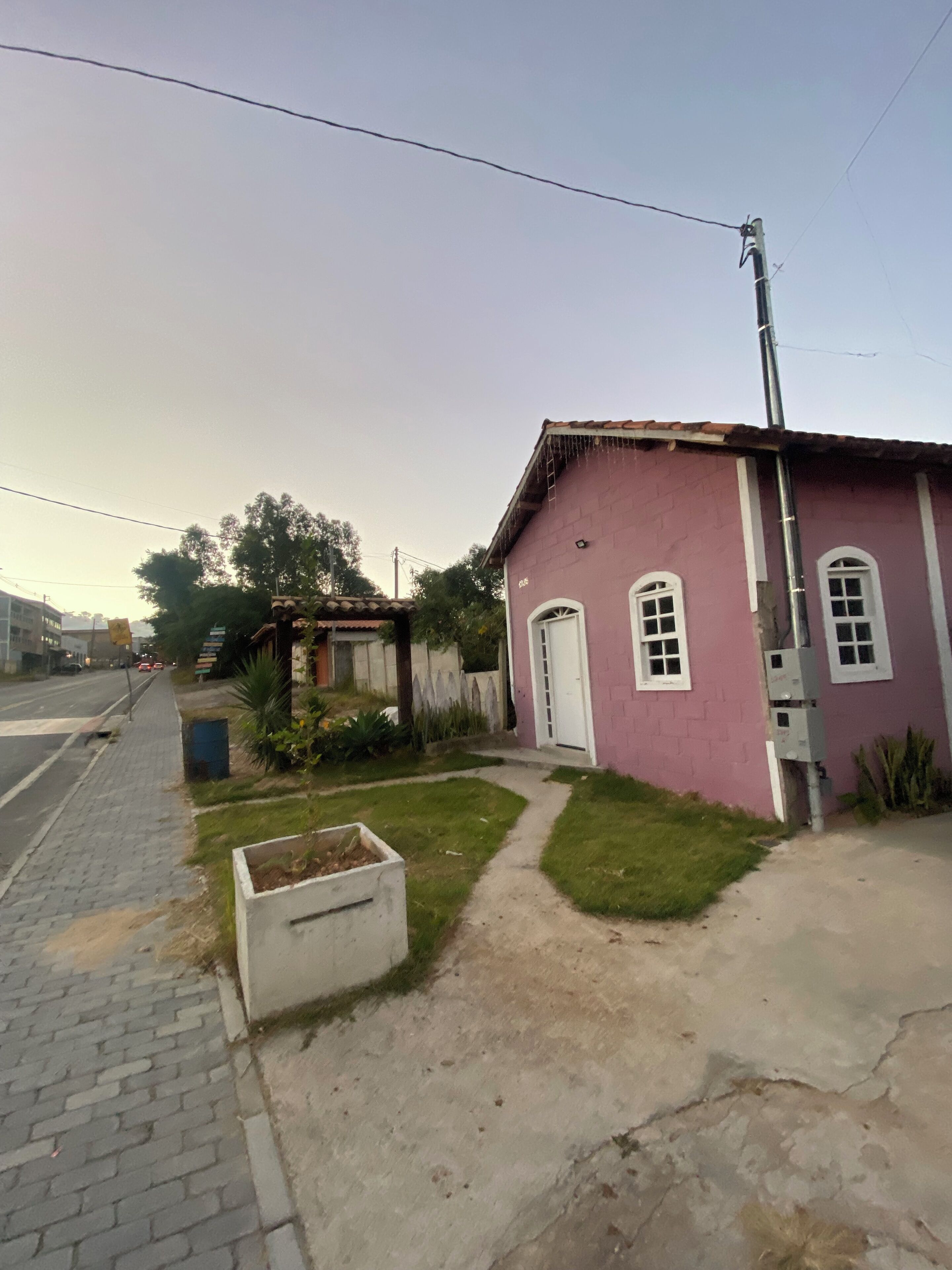 A small pink building with a white door and windows, a paved sidewalk, and a grassy area with a planter box.