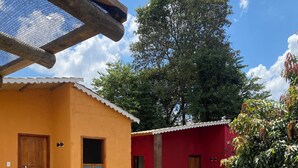 Een binnenplaats met twee gebouwen, een geel en een rood, met een grote boom en een bamboomschutting.