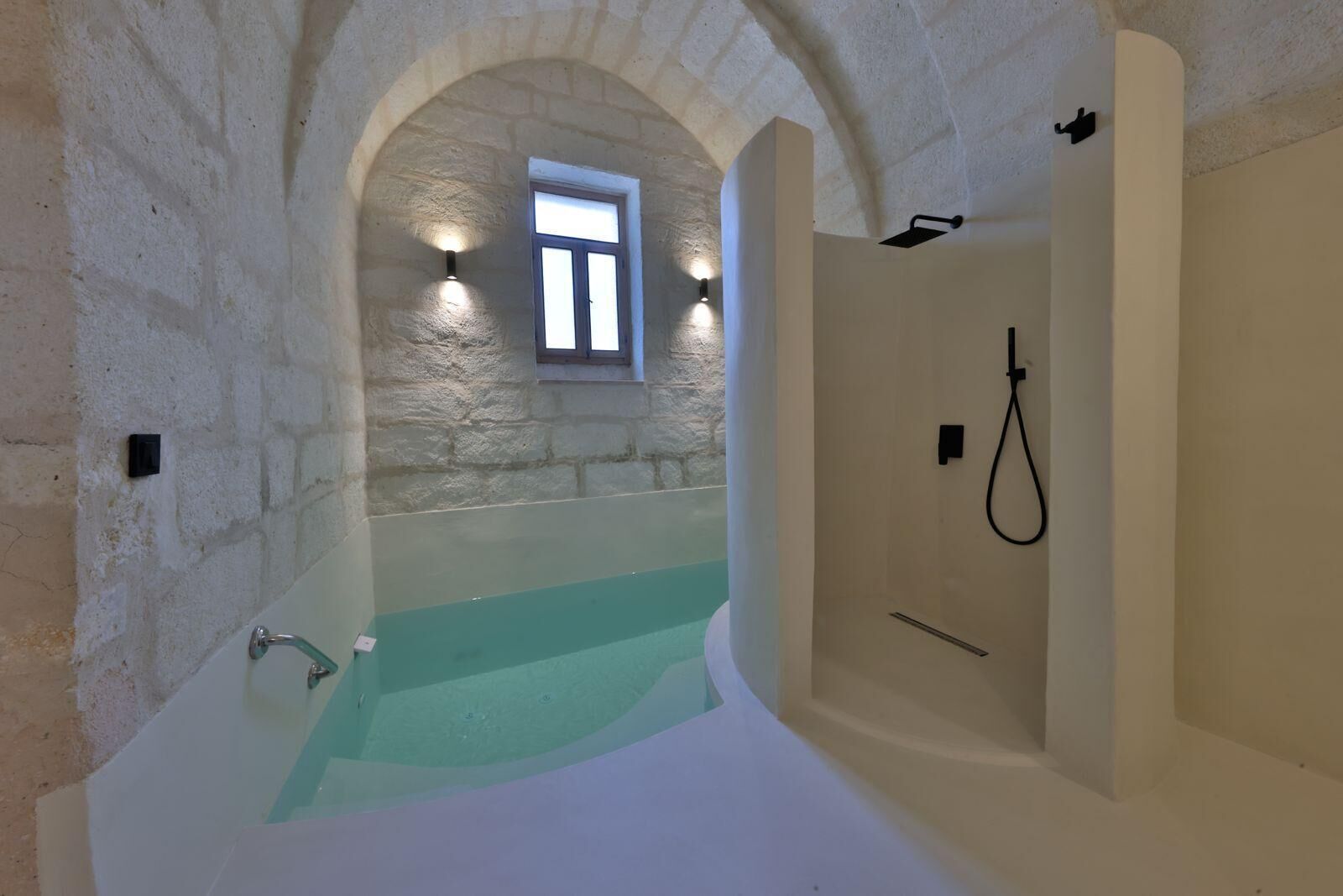A bathroom with a stone archway, a window, a bathtub, and a shower area.