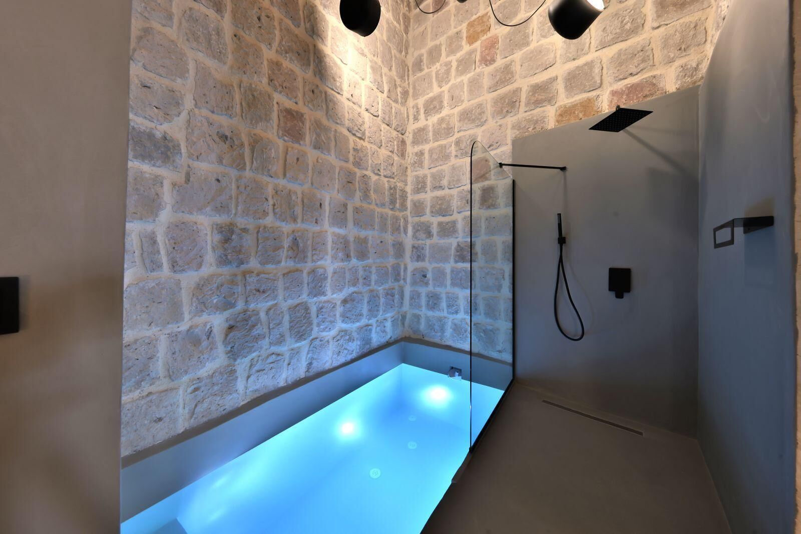 A modern bathroom with a stone wall, a glass-enclosed bathtub, and a shower area.