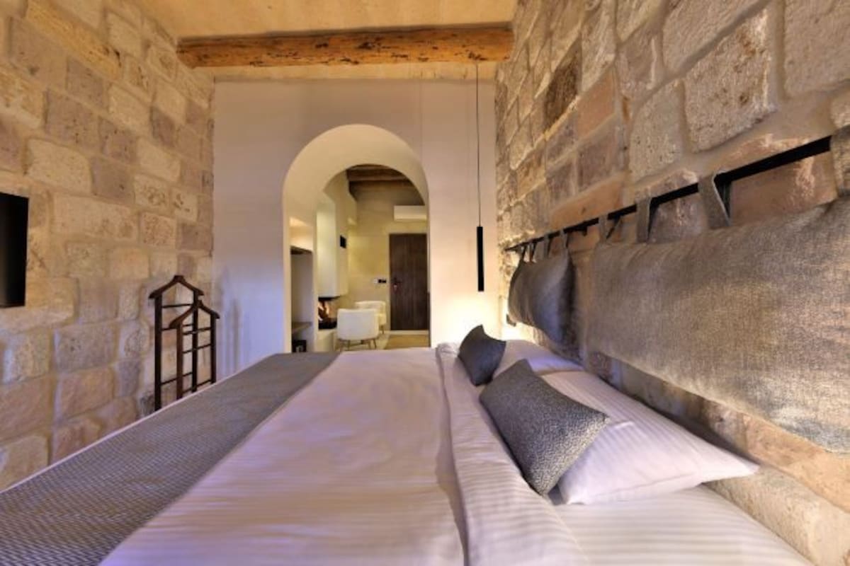 Un dormitorio con paredes de piedra, una cama con sábanas blancas y un cabecero de madera.