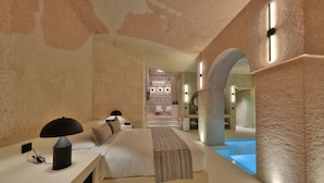 A modern hotel room with a bed, bedside table, lamp, and a view of a spa area. - Simurg Cave House (Urgup)