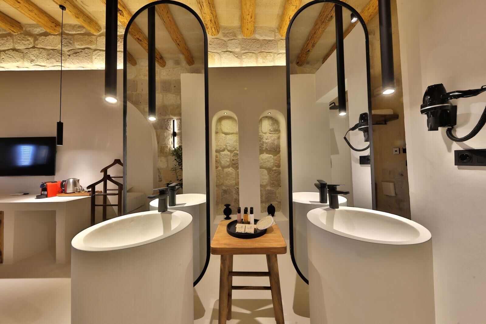Un baño moderno con dos lavamanos, un taburete de madera y un espejo.