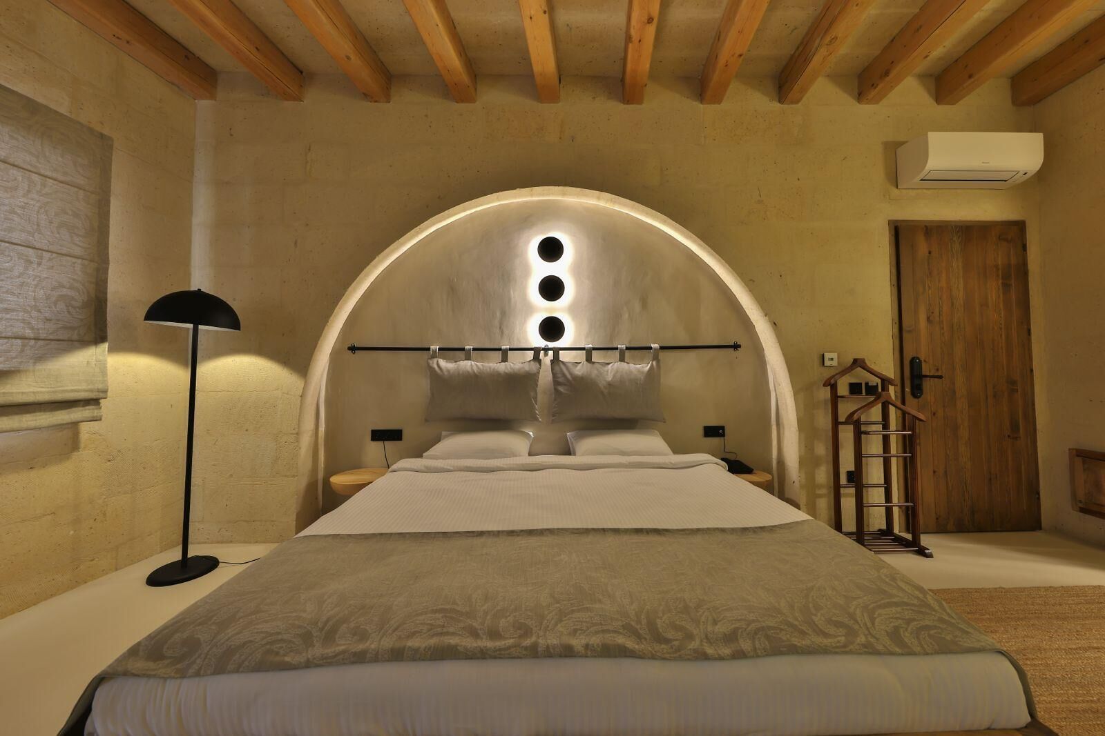 Ein Schlafzimmer mit einem großen Bett, einer Holzbalkendecke, einem Rundbogenfenster und einem Nachttisch mit einer Lampe.