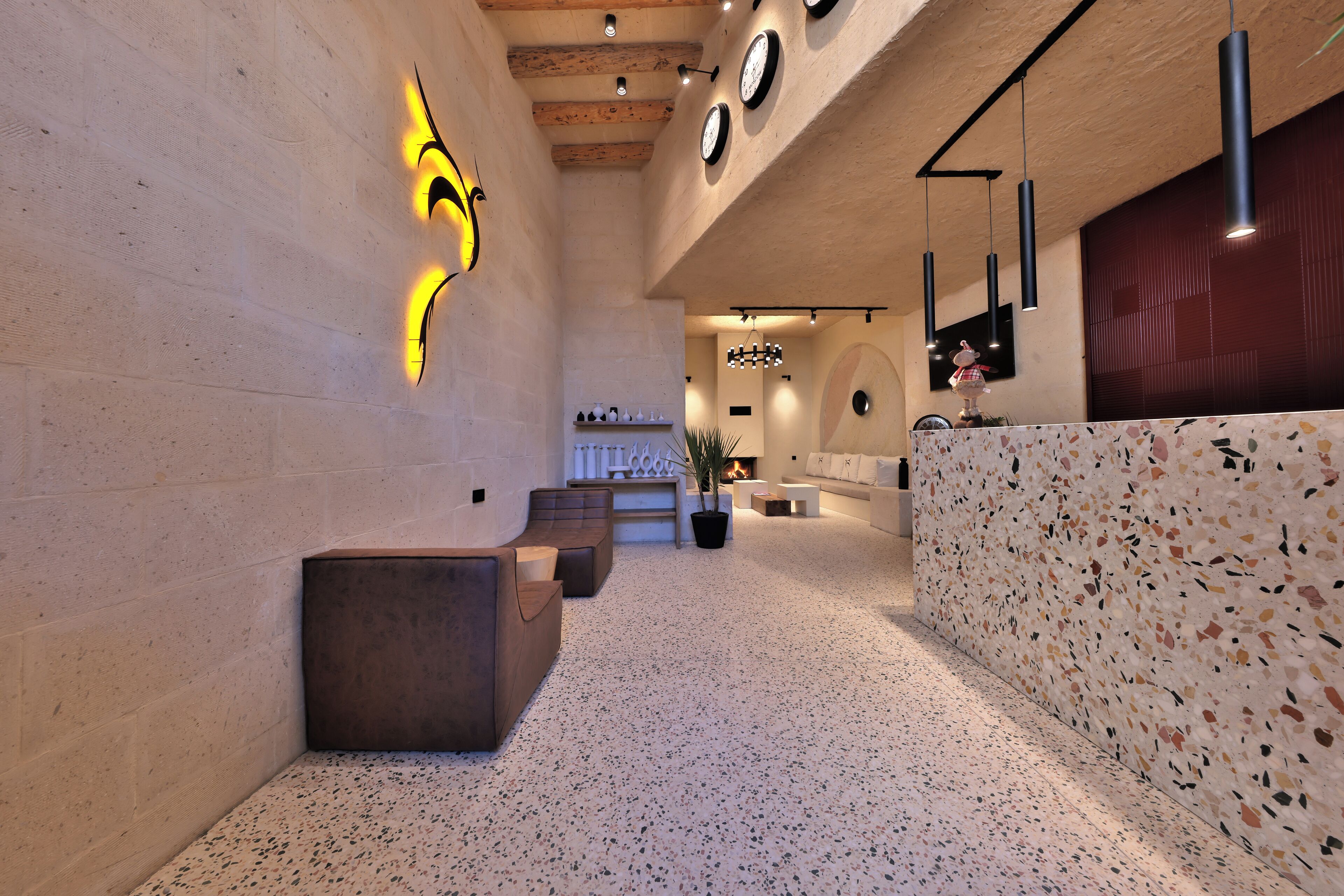A modern lobby with a reception desk, seating area, and a wall with clocks.