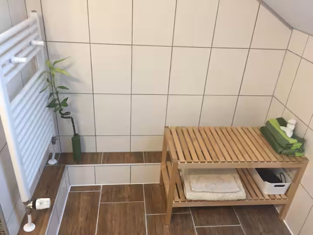 A bathroom with a wooden bench, a radiator, a plant, and a tiled floor.