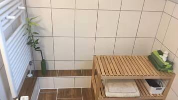 A bathroom with a wooden bench, a radiator, a plant, and a tiled floor.