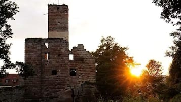 Eine historische Steinarchitektur mit einer Flagge auf dem Dach, umgeben von Bäumen und einem Sonnenuntergang im Hintergrund.