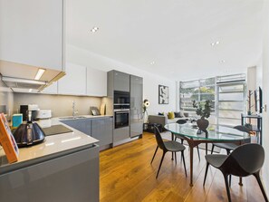 Une cuisine moderne avec un coin repas, un plancher en bois et une grande fenêtre équipée de stores.