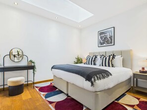 Une chambre à coucher moderne avec un lit, des tables de chevet, un bureau et un miroir.