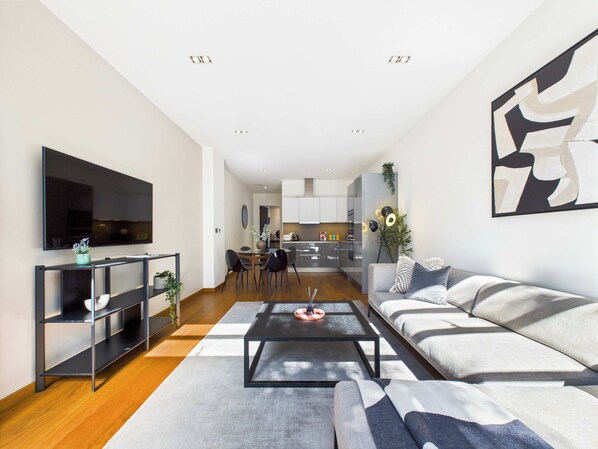 A modern living room with a sofa, coffee table, and TV. There is a kitchen in the background.