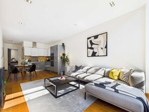 Uma sala moderna com um sofá seccional cinza, uma mesa de centro de vidro e um espaço de jantar com mesa e cadeiras de madeira escura.